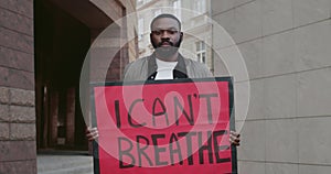 Young afro american guy holding placard with i cant breath writing. Male protestor supporting movement against police