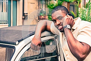 Young afro american guy speaking at mobile phone next old retro car - Black man smiling during phone conversation - Fashion with