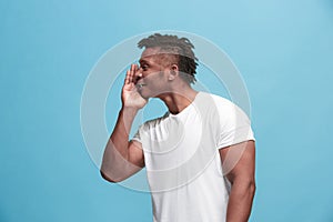 The young afro-american man whispering a secret behind her hand over blue background
