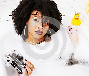 Young afro-american teen girl laying in bath with foam, wearing
