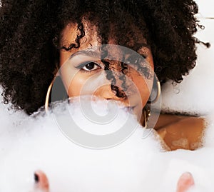 Young afro-american teen girl laying in bath with foam, wearing