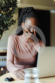 Young afro american woman laughing covering mouth and talking online on laptop in coffee house. Black girl working