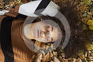 Young afro american woman lying on autumnal leaves in sunny park.