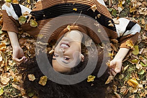 Young afro american woman lying on autumnal leaves in sunny park.