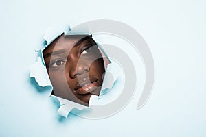 Young afro american woman with make up face skincare inside hole on blue background. Cosmetics concept