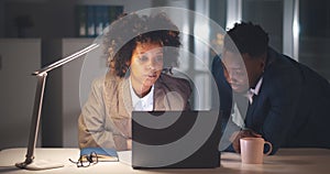 Young afro colleagues sitting together at desk working late at night in dark office on computer