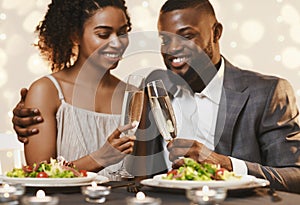 Young afro couple toasting with champagne while having dinner