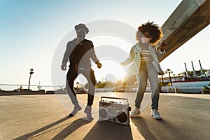 Young Afro friends wearing face mask dancing outdoor while listening to music with wireless headphones and boombox