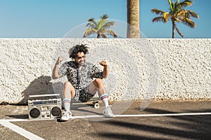 Young Afro Latin man having fun dancing while listening music with headphones and vintage boombox during summer vacation