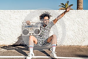 Young Afro Latin man having fun listening music with headphones and vintage boombox during summer vacation