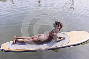 Young afro slim girl lying on paddle Board in sea