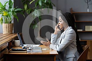 Young afro woman office worker using mobile phone, making phonecall in workplace