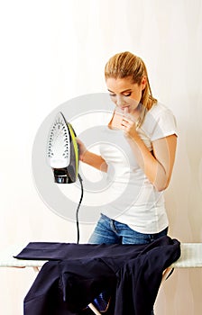 Young aghast woman standing behind ironing desk with iron in hand