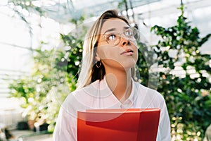 Young agricultural engineer working in greenhouse. Young female scientist looks away