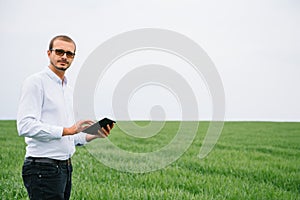 Young agronomist holds tablet touch pad computer in green wheat field. Agribusiness concept. agricultural engineer standing in a