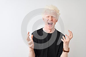 Young albino blond man wearing black t-shirt standing over isolated white background crazy and mad shouting and yelling with