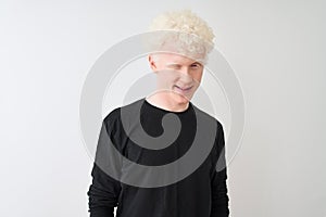 Young albino blond man wearing black t-shirt standing over isolated white background winking looking at the camera with sexy