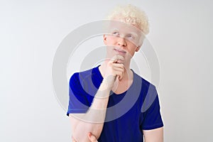 Young albino blond man wearing blue casual t-shirt standing over isolated white background with hand on chin thinking about