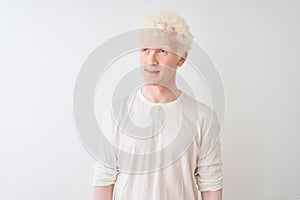 Young albino blond man wearing casual t-shirt standing over isolated white background smiling looking to the side and staring away