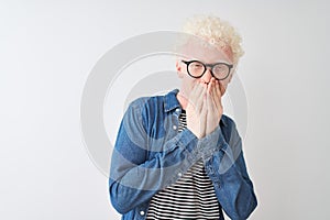 Young albino blond man wearing denim shirt and glasses over isolated white background laughing and embarrassed giggle covering
