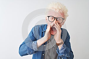 Young albino blond man wearing denim shirt and glasses over isolated white background Shouting angry out loud with hands over