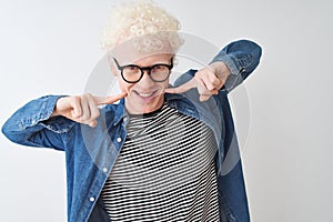 Young albino blond man wearing denim shirt and glasses over isolated white background smiling cheerful showing and pointing with