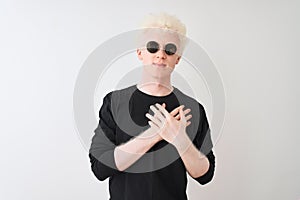 Young albino man wearing black t-shirt and sunglasess standing over isolated white background smiling with hands on chest with