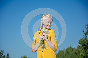 A young albino woman in a yellow blouse against a blue sky. holding a bouquet of daisies in her hands, in front of face