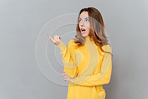 Young amazed woman in yellow sweater pointing finger away