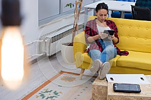 Young American business woman sitting at her sofa, using tablet in her office