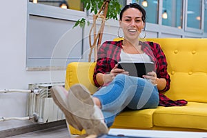 Young American business woman sitting at her sofa, using tablet in her office and smiling