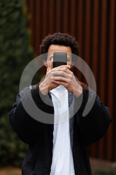 Young American guy holds smartphone in his hand, covering his face. Digital Generation Addiction concept