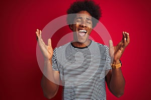 Young american man with afro hair wearing navy striped t-shirt over isolated red background celebrating mad and crazy for success
