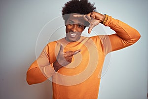 Young american man with afro hair wearing orange sweater over isolated white background smiling making frame with hands and