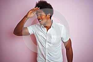 Young american man with afro hair wearing white shirt standing over isolated pink background very happy and smiling looking far