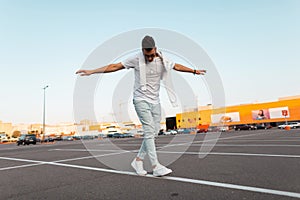 Young American man hipster keeps balance and walks along a white line on the asphalt. Attractive guy in a stylish T-shirt in