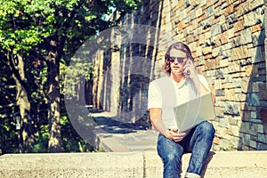 Young American Man with long hair working on laptop computer, talking on cell phone in New York City