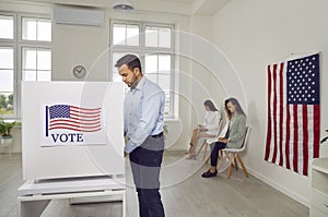 Young american voter man standing at vote center in voting booth making a choice on election day.