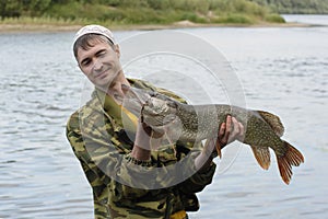 Young angler holds and looks at the big pike