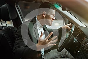 Young angry businessman sitts in his car looks anxious after hard day at workplace, stressfull working conditions concept