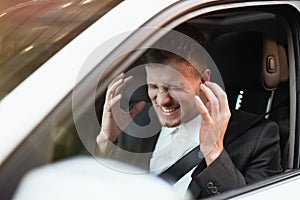 Young angry businessman sitts in his car looks desperate after hard day at workplace, stressfull working conditions concept