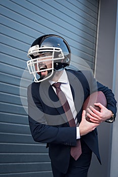 young angry businessman in suit and rugby helmet with ball in hands