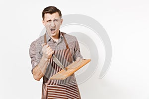 Young angry fun man chef or waiter in striped brown apron, shirt holding wooden cutting board, knife isolated on white