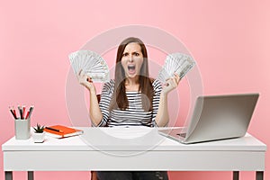 Young angry irritated woman scream spread hands with bundle lots of dollars cash money work at office at white desk with