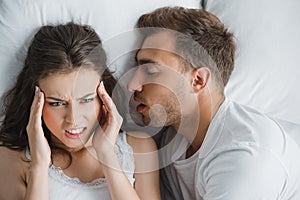 young angry woman having headache while lying with snoring husband