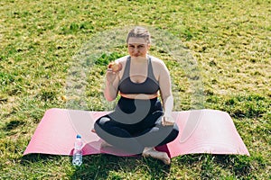 Young angry woman wearing sportswear eating apple outdoors. Fat woman dieting, fitness and healthy food on nature