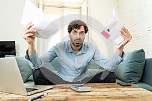 Angry man paying bills as home with laptop and calculator