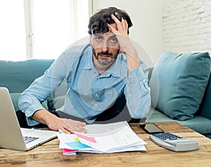 Angry man paying bills as home with laptop and calculator