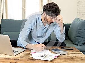 Angry man paying bills as home with laptop and calculator