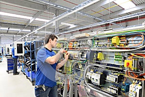 young apprentice assembles components and cables in a factory in a switch cabinet - workplace industry with future